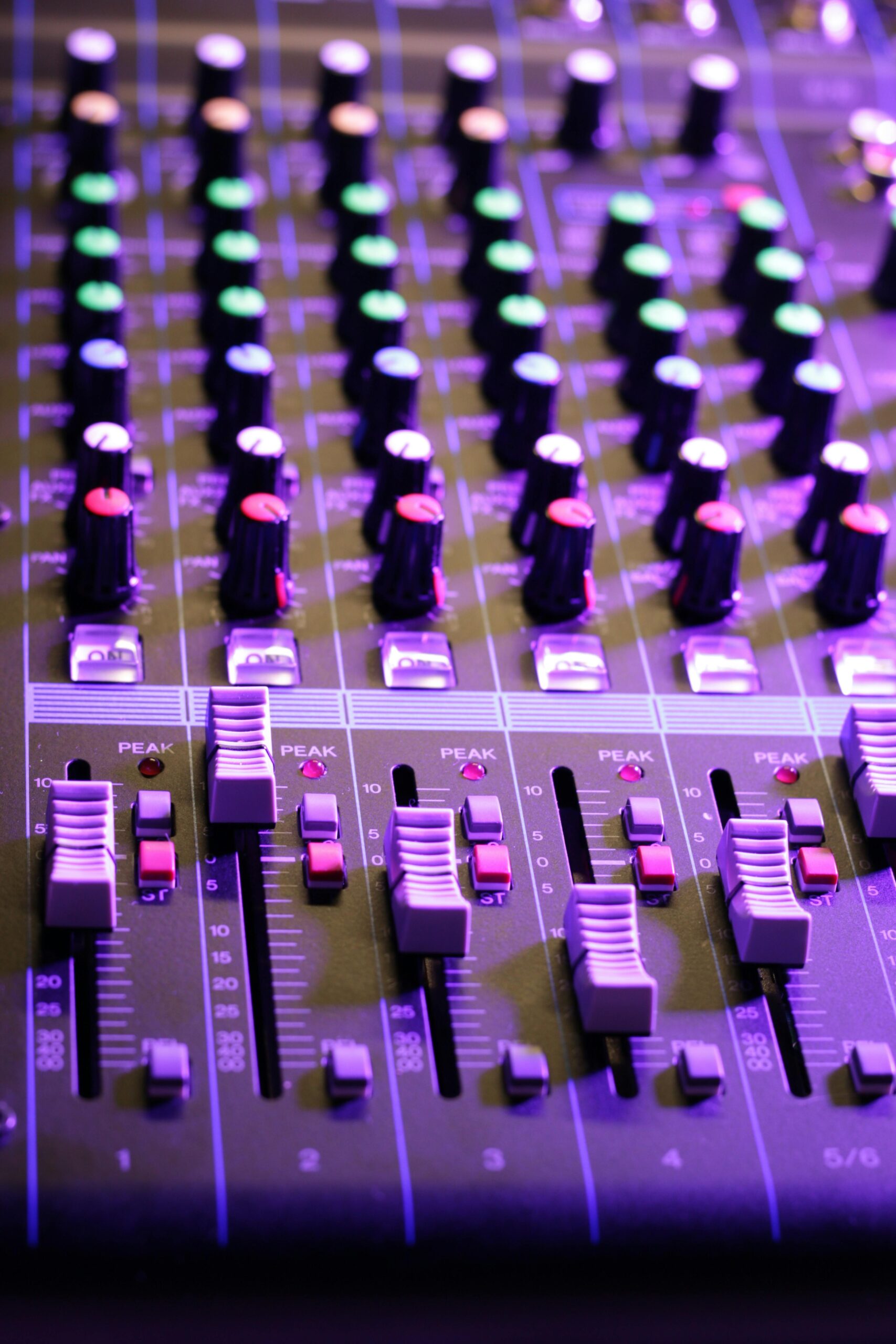Vertical close-up of an audio mixer with vibrant knobs and sliders. Ideal for music tech themes.